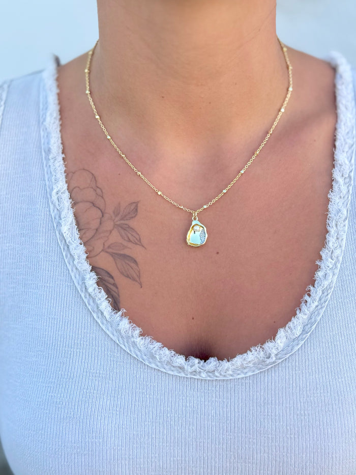 Gold necklace with a pendant featuring a pearl in a golden oyster being worn