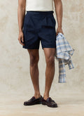 Navy cotton Blake Double Pleated Shorts by Percival, styled on a model with loafers and a blue checked shirt.