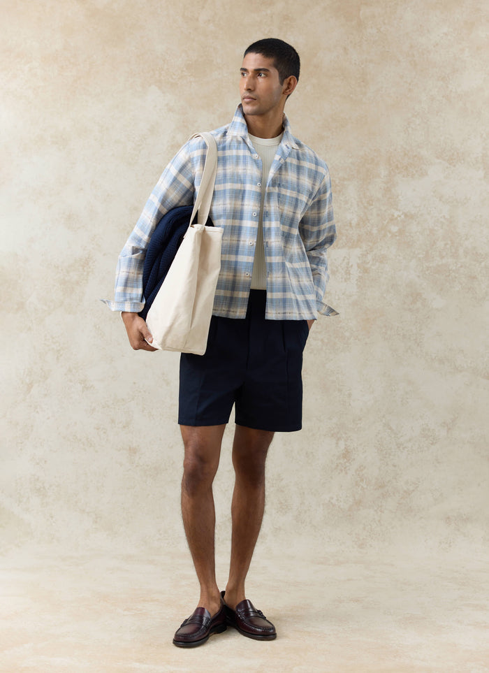 Navy Percival Blake double pleated cotton shorts styled with a blue checked shirt and a cream Gordon tote bag.