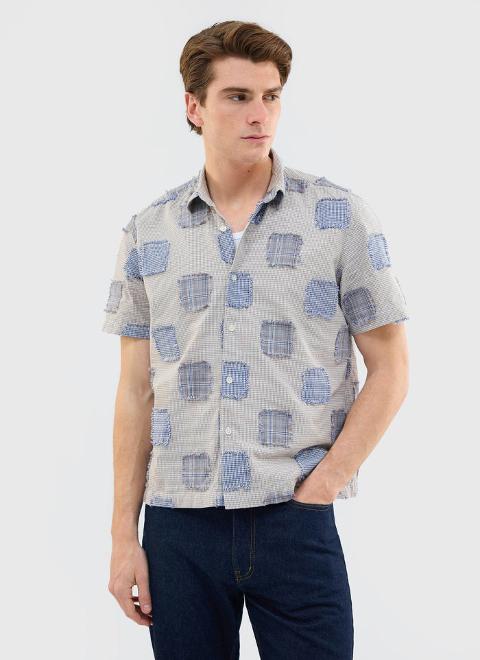 A man models the Percival Bruno Boxy Clerk Shirt in grey, a short-sleeve shirt with a unique patchwork design.
