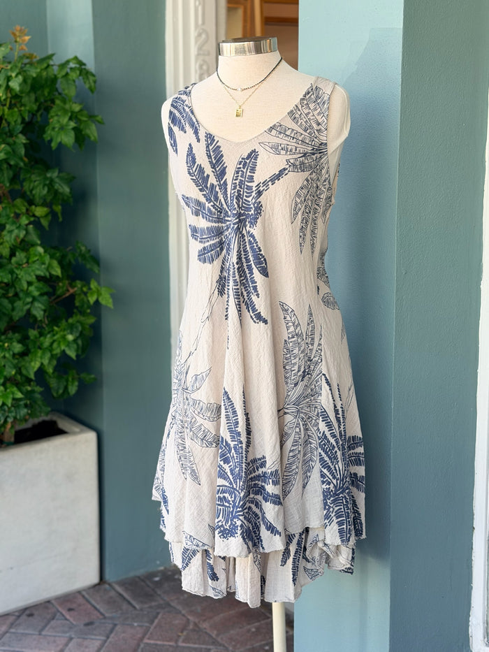 Sleeveless taupe dress with navy palm print, featuring a flowy layered hem and lightweight fabric, displayed on a mannequin.