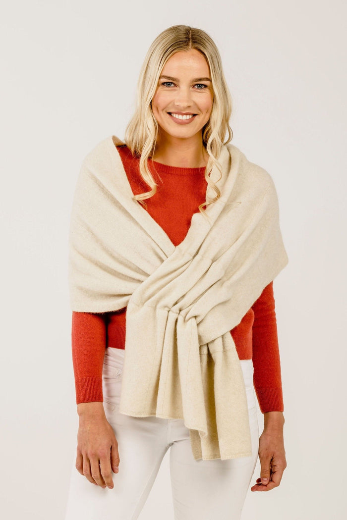 A woman wearing a cream-colored cashmere stole with a subtle texture, draped over her shoulders. She is also wearing a red top and white pants.