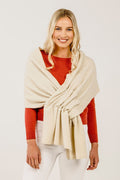 A woman wearing a cream-colored cashmere stole with a subtle texture, draped over her shoulders. She is also wearing a red top and white pants.