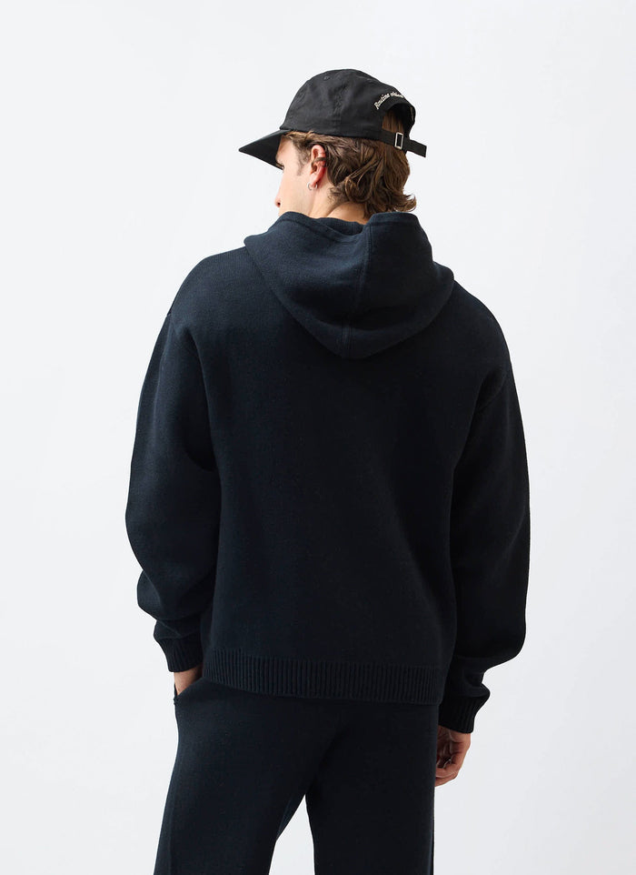 The back view of a model wearing the Percival Chronicle Knitted Hoodie in black, showing the oversized fit and hood.