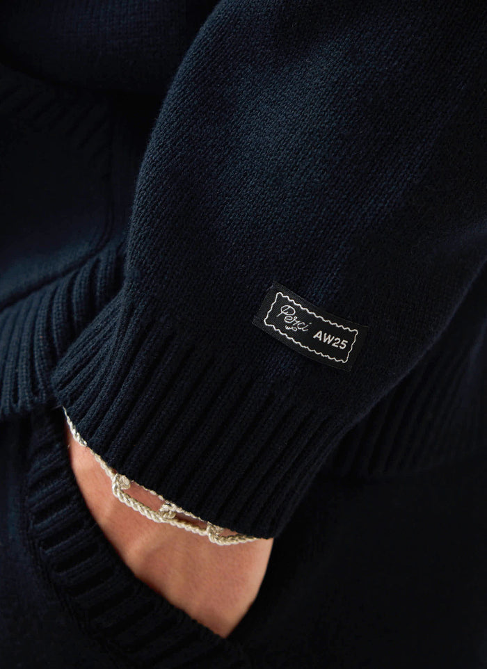 Close-up detail of the woven Percival AW25 label on the ribbed sleeve of the black cotton Chronicle Knitted Hoodie.