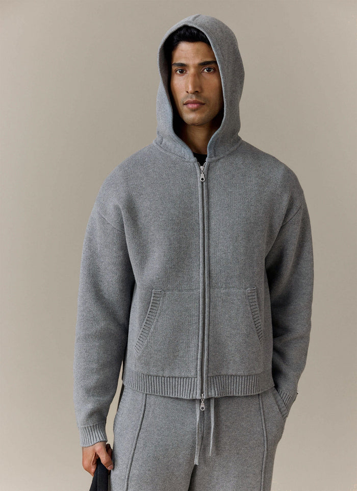 A model wears the grey Chronicle Knitted Hoodie from Percival with the hood up, looking directly at the camera.