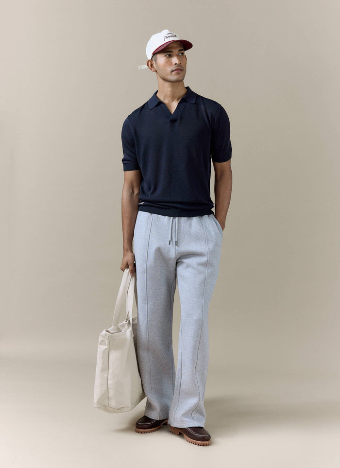 Navy Laurence Knitted Polo by Percival in a linen-lyocell blend, worn by a model with grey trousers and a cap.