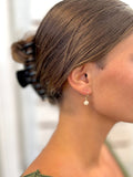 Close-up of a person's ear with a hair clip and pearl earring against a blurred background