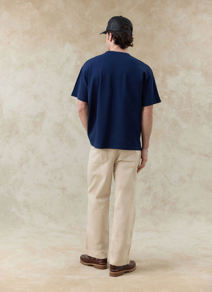 Navy Percival Clarke embroidered organic cotton t-shirt, seen from the back with beige trousers from the SS26 range.
