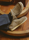 Close-up of a person wearing smoke grey suede Clarks Wallabees from Percival, styled with dark denim trousers.