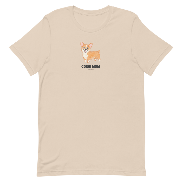 The Sassy Woof Corgi Mom Tee is a beige shirt with a cute corgi illustration and "Corgi Mom" text—perfect for corgi lovers.