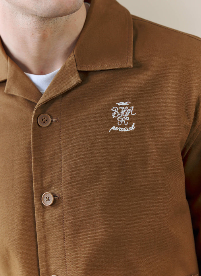 A close-up of the white embroidered logo on the chest of the Percival x Brighton & Hove Albion FC Canvas Workshirt in brown.