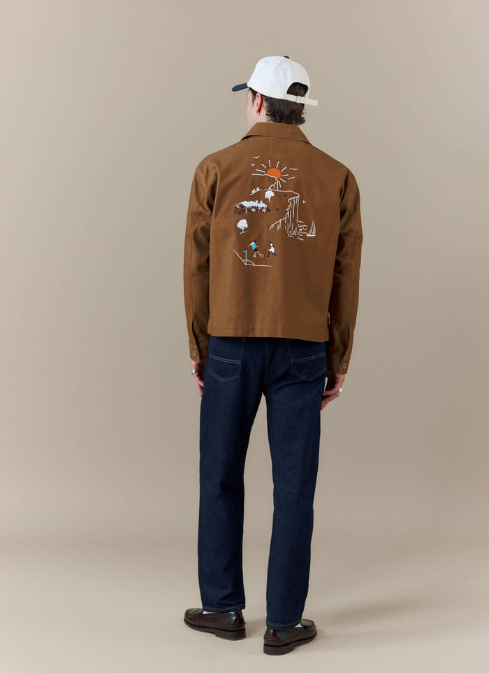 A back view of a model wearing the brown Percival x Brighton & Hove Albion F.C. workshirt with its landscape embroidery.