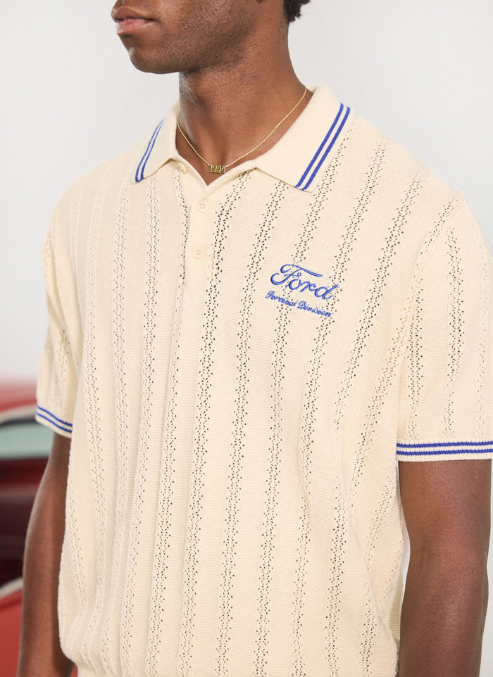 Close-up of a model wearing the Percival x Ford dealership knitted polo in ecru with blue embroidery and collar tipping.