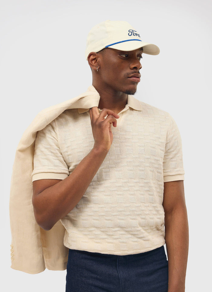 A model wears the Percival Deck Negroni Knitted Shirt in ecru, with a matching jacket slung over his shoulder.