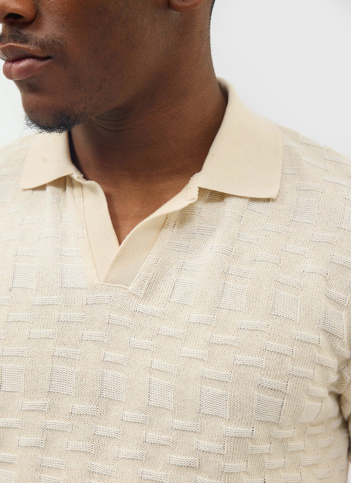 A close-up of a model wearing the ecru Deck Negroni Knitted Shirt from Percival, showing the textured cotton knit and collar.
