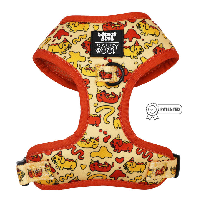 The Sassy Woof Dog Adjustable Harness - Hot Dawg features red trim, a cartoon dog, heart, and bone pattern in yellow and red, plus a “Sassy Woof” label and “Patented” badge—perfect for weenie dog fans.
