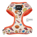 The Shell Yeah Dog Adjustable Harness by Sassy Woof features a colorful seashell pattern, orange trim, front logo patch, puppy growth protection, and a patented badge on the right side.