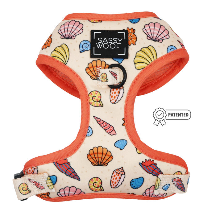 The Shell Yeah Dog Adjustable Harness by Sassy Woof features a colorful seashell pattern, orange trim, front logo patch, puppy growth protection, and a patented badge on the right side.