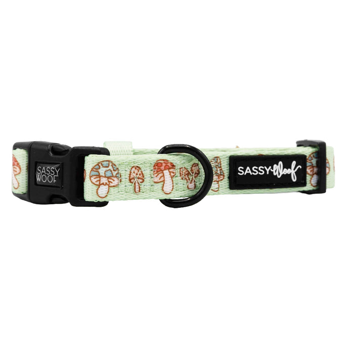 The Sassy Woof Dog Collar - Shrooms & Blooms features a light green, adjustable fit with brown and beige mushroom pattern, black plastic buckle, metal D-ring, and signature label. Ideal for pups in the Puppy Growth Pawtection Plan!.
