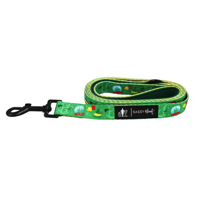 A green dog collar from the Sassy Woof Dog Collar Three Piece Bundle - Elf™, featuring a black clasp, festive Christmas-inspired patterns, and branded with a Sassy Woof fabric label.