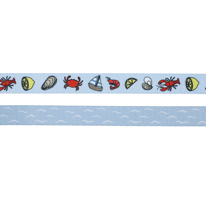 The Sassy Woof Dog Leash - Coastal Cuties features a light blue ribbon with crabs, lemons, clams, shrimp, sailboats, and shells in a repeating pattern. It coordinates with the matching adjustable harness ribbon adorned with small white wave designs.