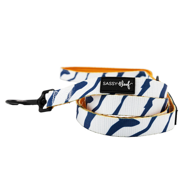 The Sassy Woof Dog Leash - STAR WARS™ Ahsoka features blue and white wavy stripes, a black metal clasp, signature logo tag, and an orange inner side—ideal for pairing with an adjustable harness.