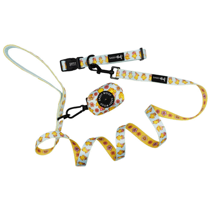 The Sassy Woof "Dog Three Piece Bundle - Good Duck, Babe!" includes a playful yellow and white cartoon duck leash, a matching collar with pink flowers, and a black clip-on waste bag holder—perfect for puppy walks.