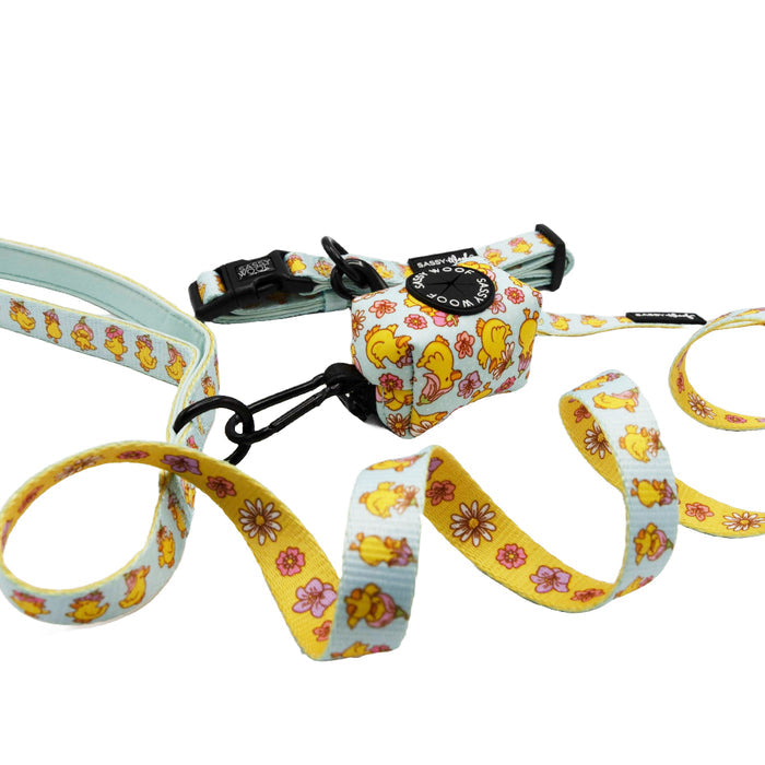 The Sassy Woof "Dog Three Piece Bundle - Good Duck, Babe!" set includes a collar, leash, and waste bag holder with cheerful yellow duck and flower patterns on white and yellow—perfect for your puppy's growth plan.