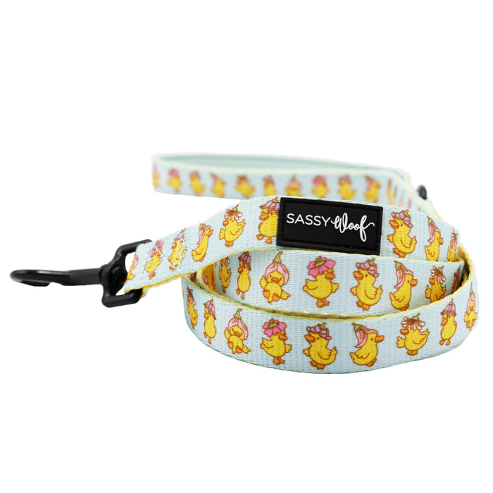 The Sassy Woof Dog Three Piece Bundle - Good Duck, Babe! includes a light blue leash with yellow ducks in pink bows and flowers, a black metal clasp, “SASSY WOOF” label by the handle, and coordinates perfectly with the matching collar.