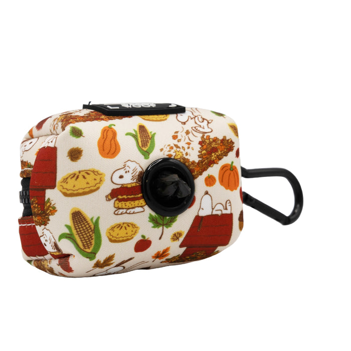 The Sassy Woof Dog Waste Bag Holder - Peanuts™ Harvest is a small, rectangular black dispenser with a clip, featuring autumn pies, pumpkins, and Snoopy on his red doghouse—a cute addition to your Peanuts dog accessories.