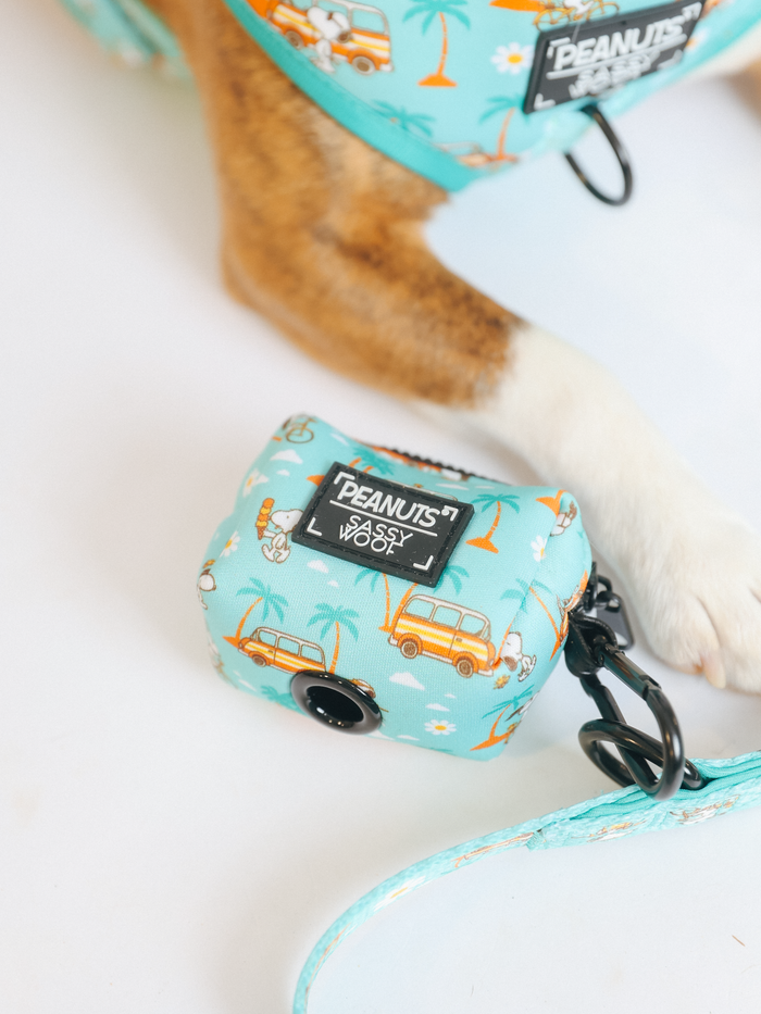 The Sassy Woof Dog Waste Bag Holder - Peanuts™ Road Tripping features a tropical van and palm tree print, easily attaches to any harness or leash, making it perfect for adventures with your dog.