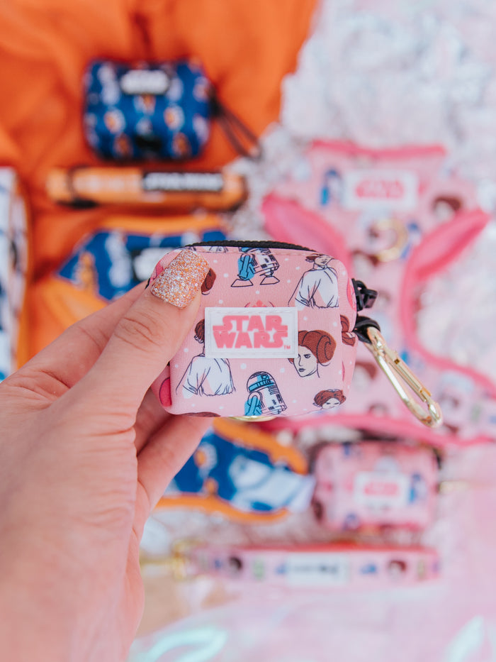 A hand holds the Sassy Woof Dog Waste Bag Holder - STAR WARS™ Princess Leia, a small pink accessory from the Star Wars collection.