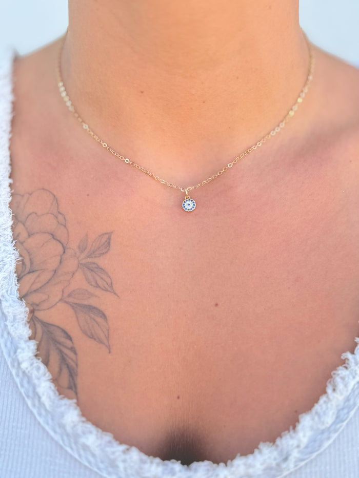 Gold necklace with a blue gemstone pendant on a white background