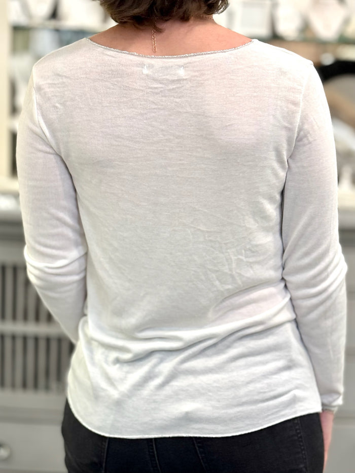 Back view of a soft white knit top with a rounded hem and smooth fit, worn with dark denim.