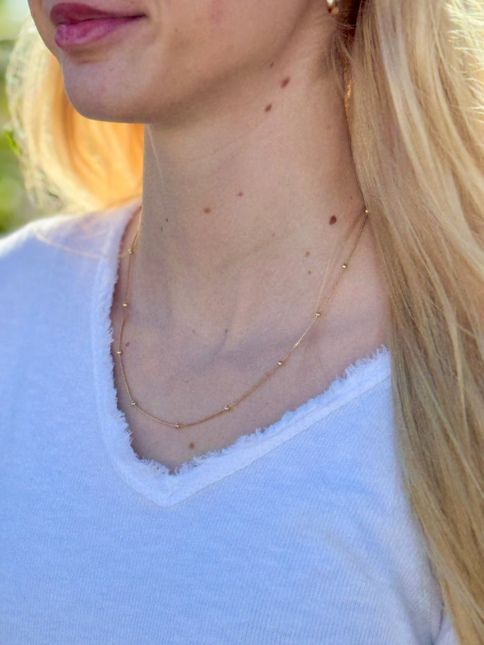 Close-up of a person wearing a delicate gold necklace with a blurred background