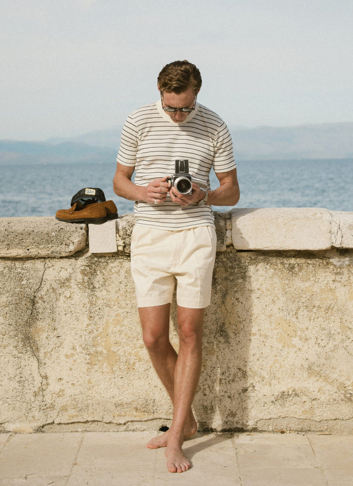 Model wearing the textured Percival Ernie Waffle T-shirt in cream stripe and Blake shorts in a coastal setting.