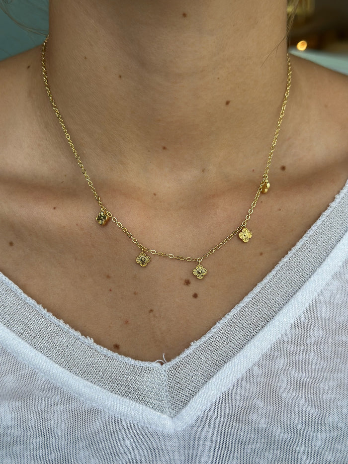 Gold necklace with small pendants on a person wearing a white shirt.