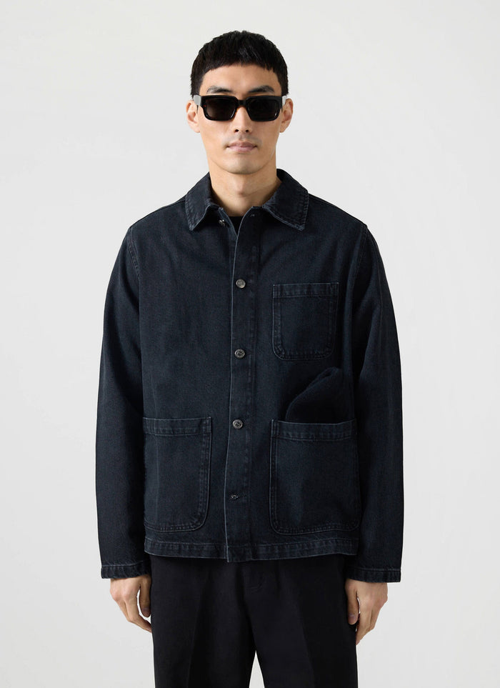 Front view of a model wearing the Percival Gove Chore Jacket in black denim, styled with black sunglasses.