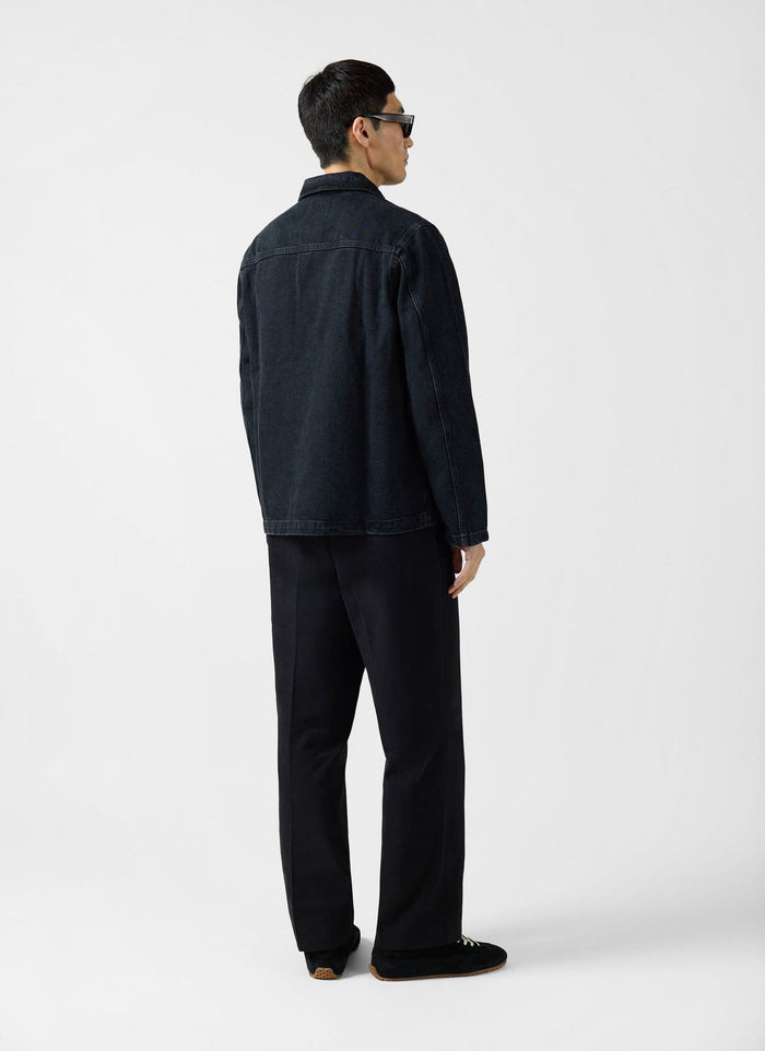 A man models the back of the Percival Gove Chore Jacket in black denim against a plain white background.