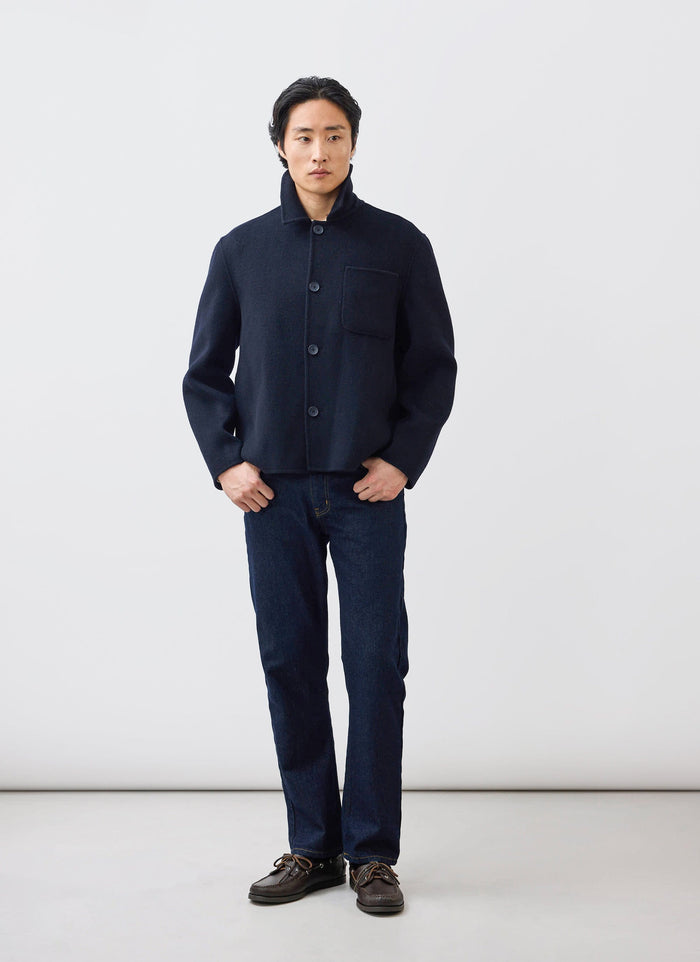 A man models the Percival Heavy Wool Overshirt in navy, paired with dark jeans and boat shoes in a studio.