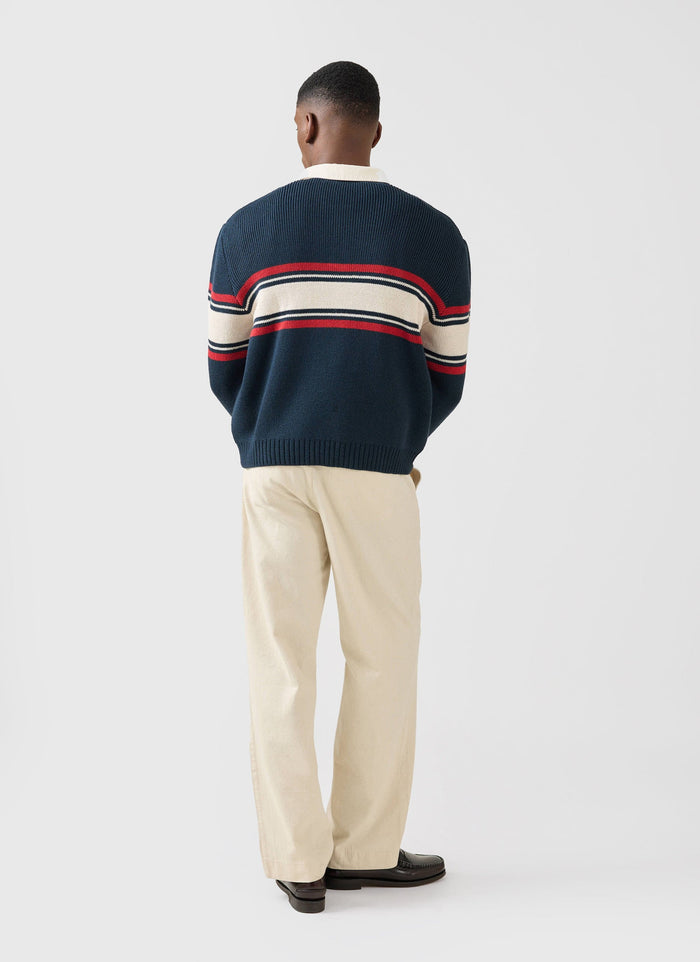 Back view of a model wearing the navy Champion x Percival Jacquard Knitted Rugby Polo Shirt, styled with cream trousers.