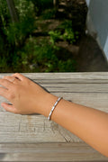 White enamel and gold cuff bracelet with crystals worn on wrist, outdoors on a wooden surface.