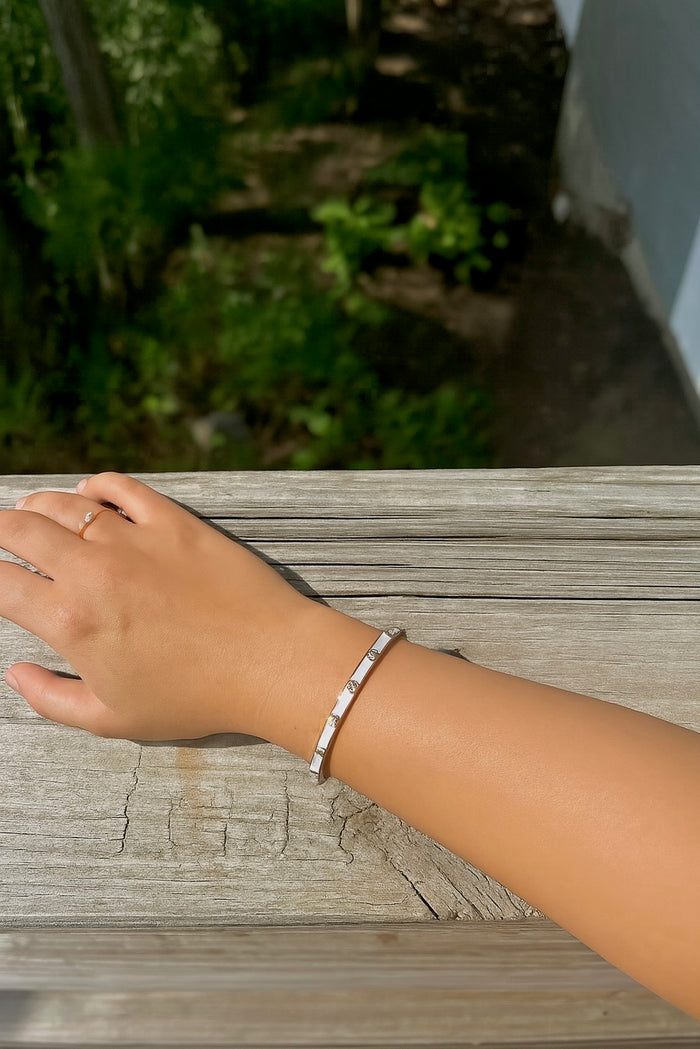 White enamel and gold cuff bracelet with crystals worn on wrist, outdoors on a wooden surface.