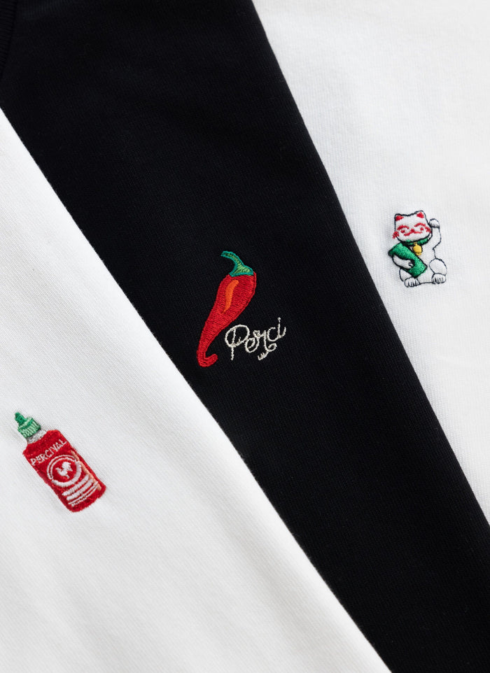 A close-up of the detailed embroidery on the Percival Loyalty T-shirts, featuring a chilli, a lucky cat and hot sauce.