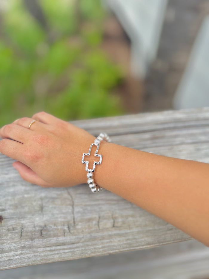 Silver beaded stretch bracelet with polished cross charm on a woman's arm