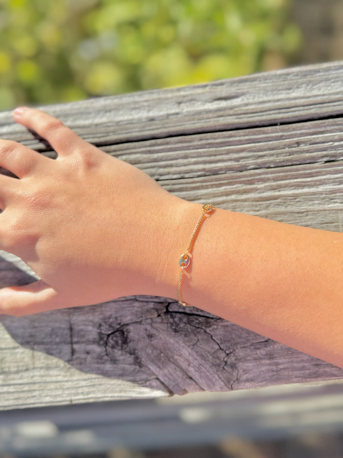 Hand wearing a bracelet on a wooden surface with a blurred natural background