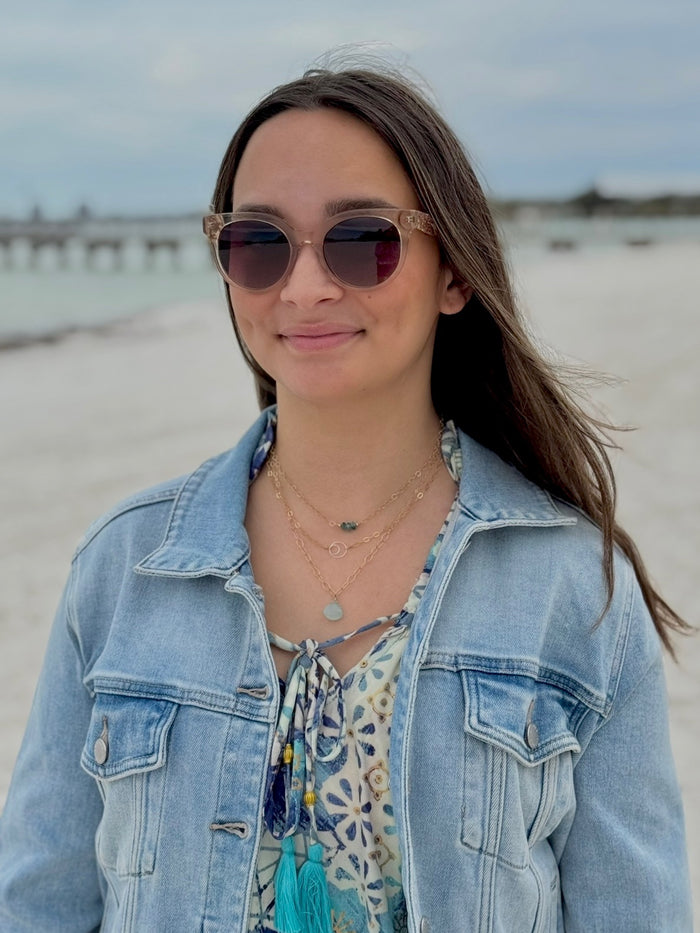 Woman wearing sunglasses and a denim jacket on a beach