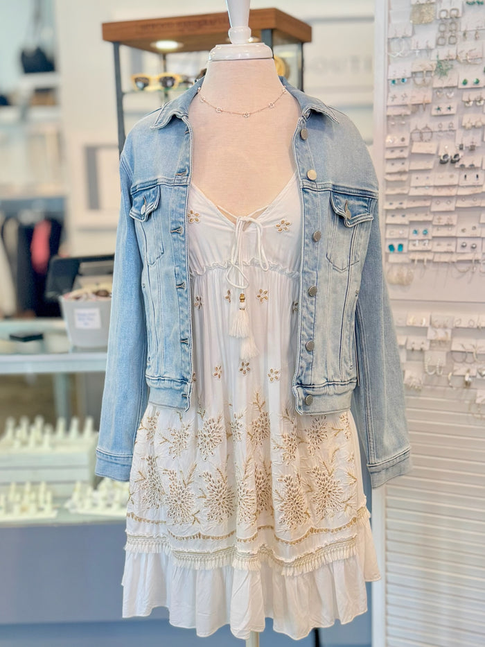 Mannequin wearing a light blue denim jacket over a white dress in a store setting.