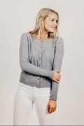 Woman wearing a gray cardigan and white pants against a plain background